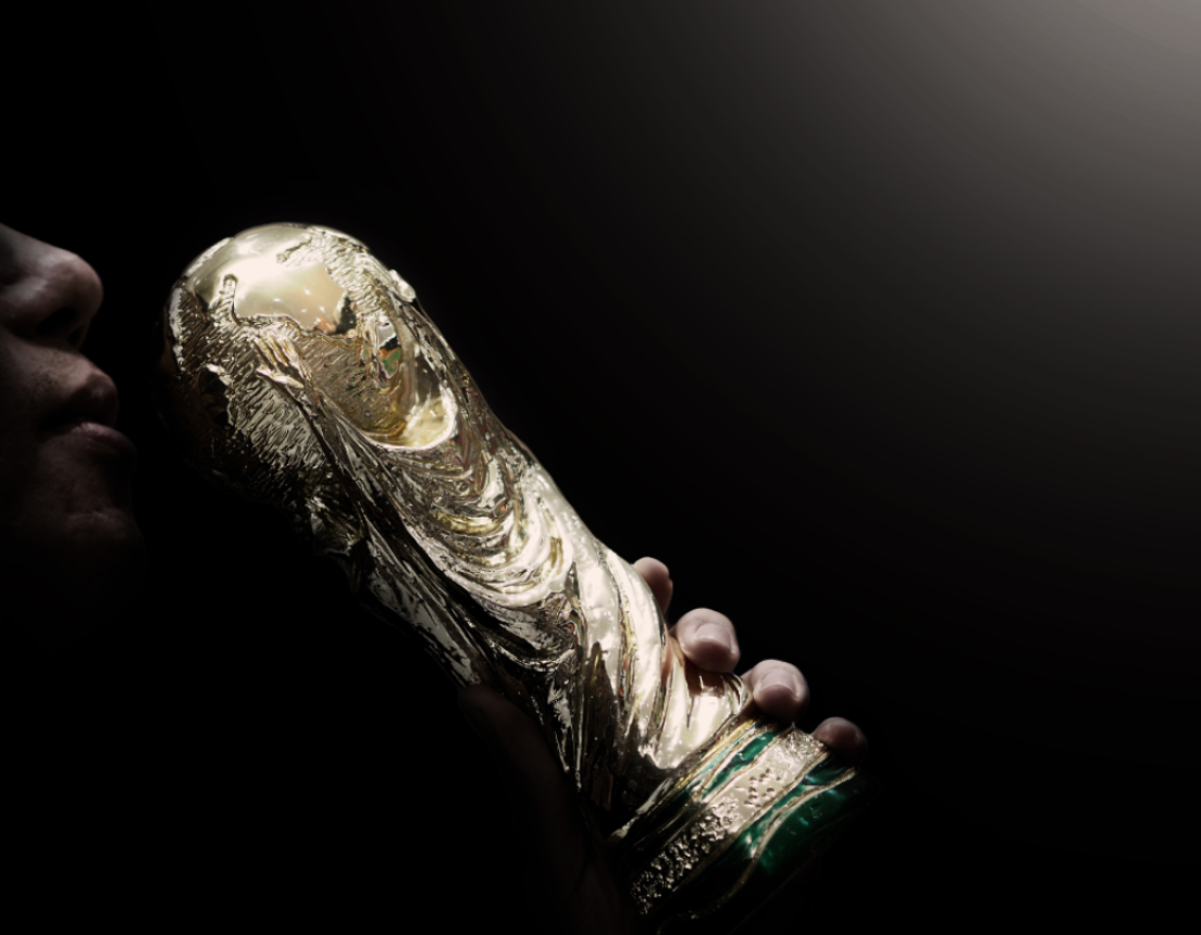 Person kissing World Cup Trophy against black background.