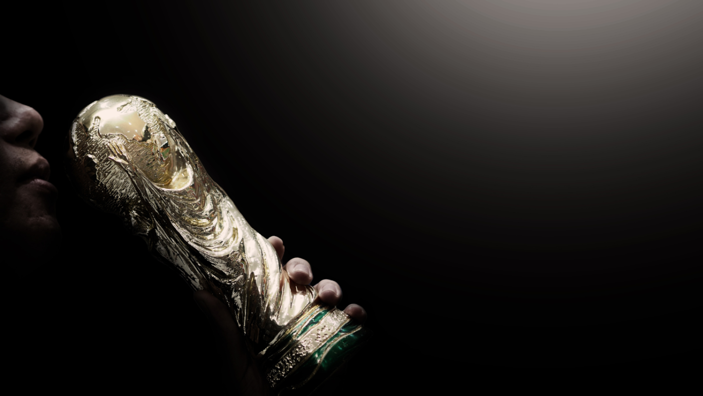 Person kissing World Cup Trophy against black background.