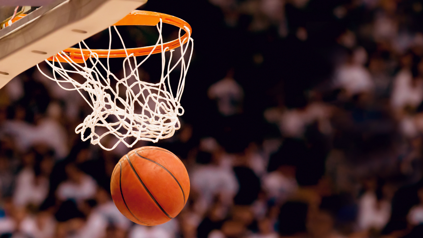 Image of a basketball going through a net against a background of fans.