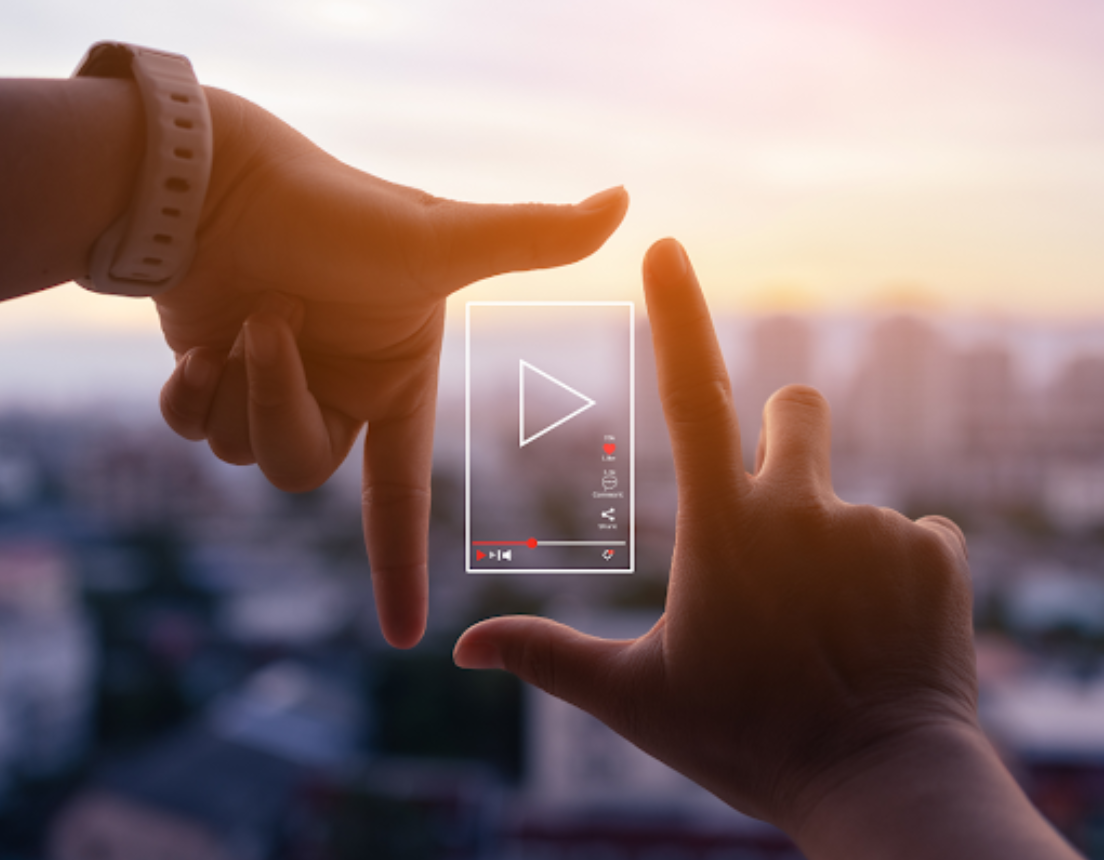 A person's thumb and index fingers forming a square with both hands, with a play button in the middle.