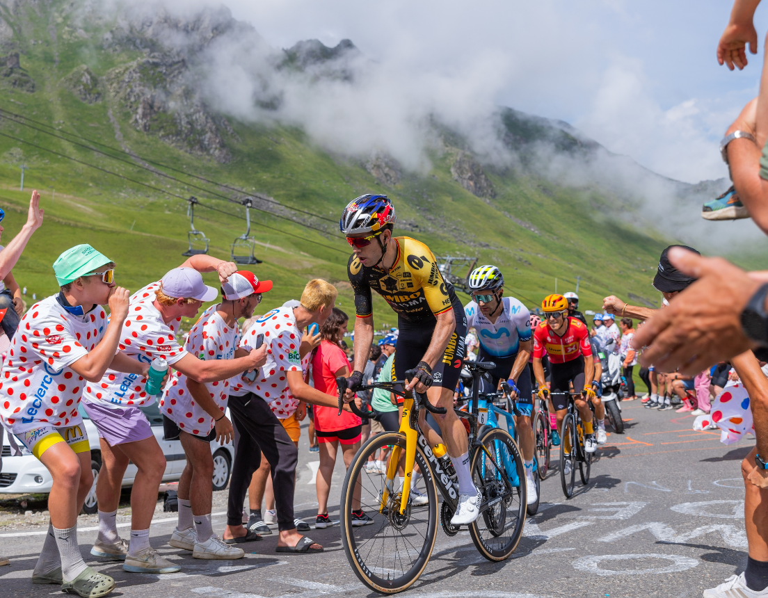 Racers competing in Tour de France scaling hill with cheering onlookers