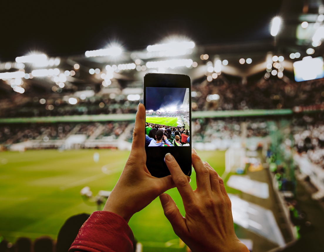 Football fan taking a vertical photo with their phone.