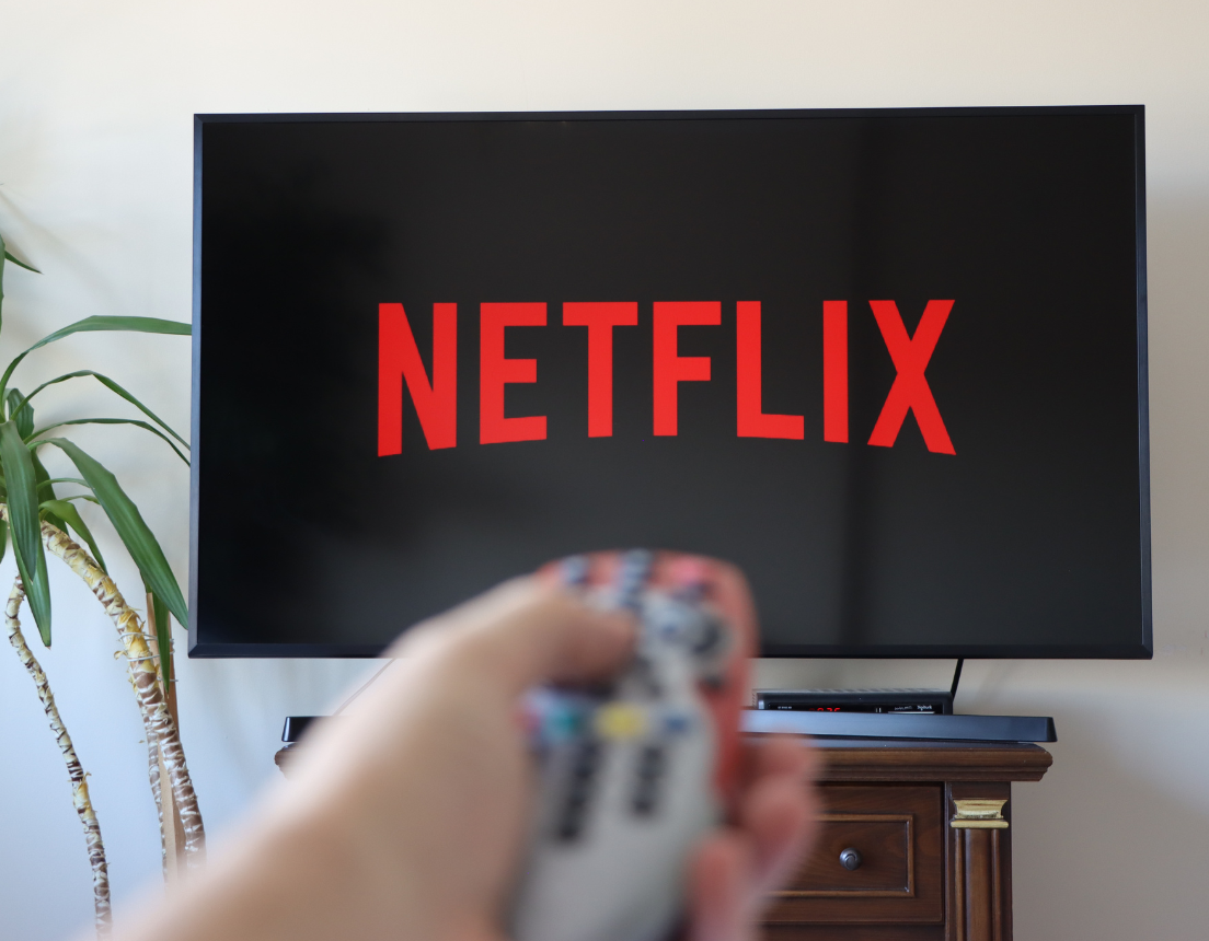 Person using remote control to turn on Netflix. With opening screen and logo appearing on television.